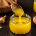 Glass jar of golden ghee and spoon on wood, homemade ghee shelf life guide