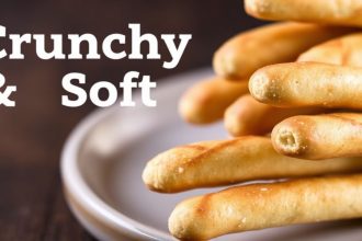 Golden crunchy and soft Breadsticks stacked on a wooden board, sprinkled with herbs.