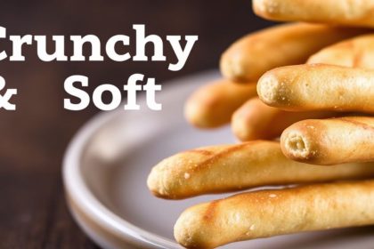 Golden crunchy and soft Breadsticks stacked on a wooden board, sprinkled with herbs.