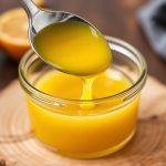 Golden Homemade Ghee in jar with spoon on wooden board, warm light highlighting clarity