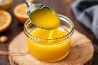 Golden Homemade Ghee in jar with spoon on wooden board, warm light highlighting clarity