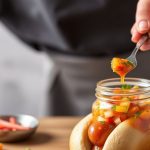 صلصة الهوت دوغ المنزلية الملونة في وعاء صغير بجانب سندويتش هوت دوغ