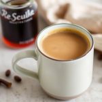 مبيض قهوة الفانيليا المصنوع منزلياً بجانب كوب قهوة وحبات فانيليا