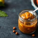 جرة تشاتني التفاح الحامض اللذيذ مع ملعقة خشبية وشرائح تفاح